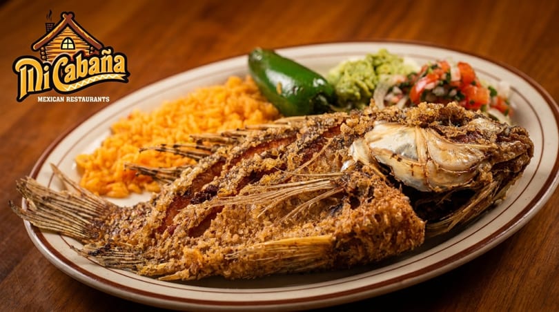 Whole fried fish with rice, jalapeño, guacamole, and pico de gallo on a plate.