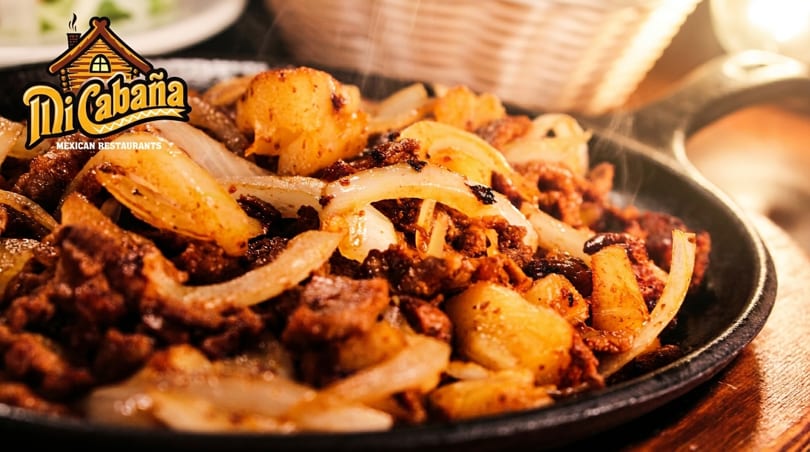 Sizzling Mi Cabaña Mexican chorizo and potatoes with onions on a hot cast iron plate.
