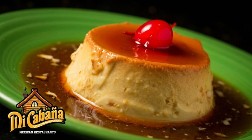 Flan dessert with caramel sauce and a cherry on top, served on a green plate.