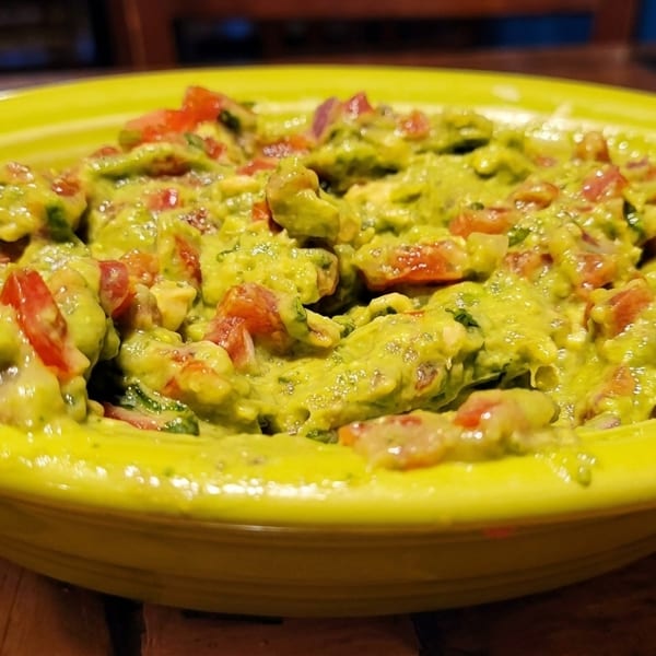 Close-up of a bright green bowl filled with chunky guacamole, featuring visible diced tomatoes and onions.