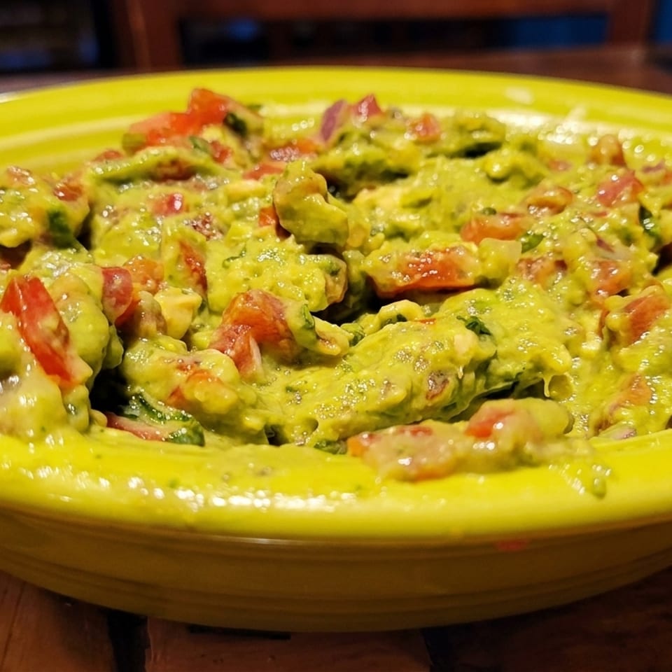 Close-up of a bright green bowl filled with chunky guacamole, featuring visible diced tomatoes and onions.