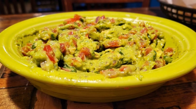Close-up of a bright green bowl filled with chunky guacamole, featuring visible diced tomatoes and onions.