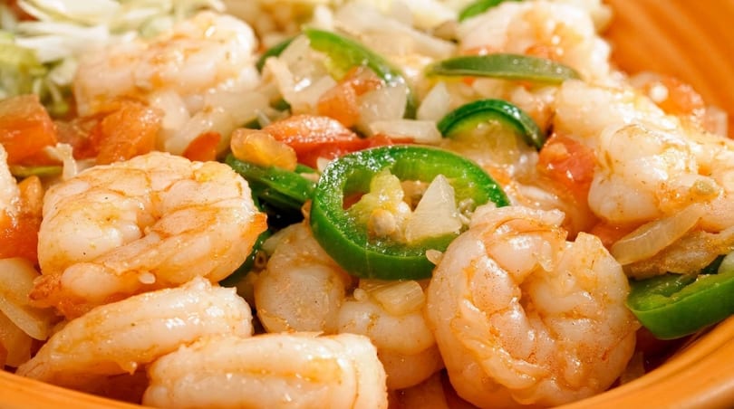 Close-up of shrimp with sliced green peppers, onions, and tomatoes in an orange bowl.