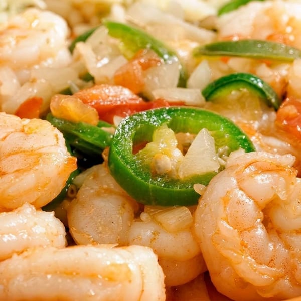 Close-up of shrimp with sliced green peppers, onions, and tomatoes in an orange bowl.
