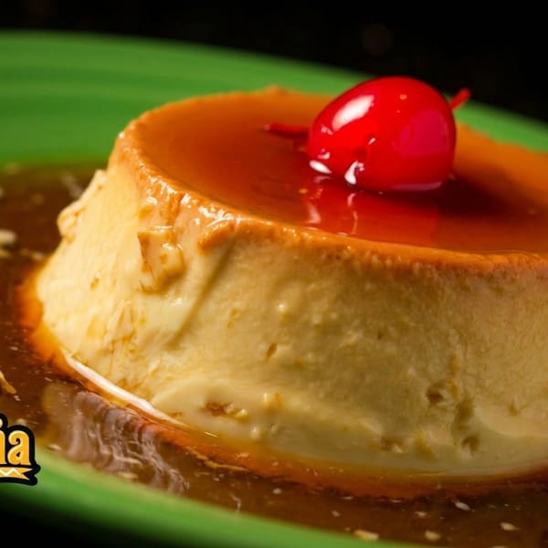 Flan dessert with caramel sauce and a cherry on a green plate from Mi Cabaña Mexican Restaurants.