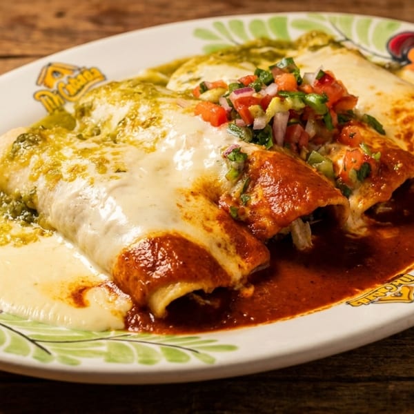 Three enchiladas, two with red sauce and one with green sauce, topped with cheese and pico de gallo.