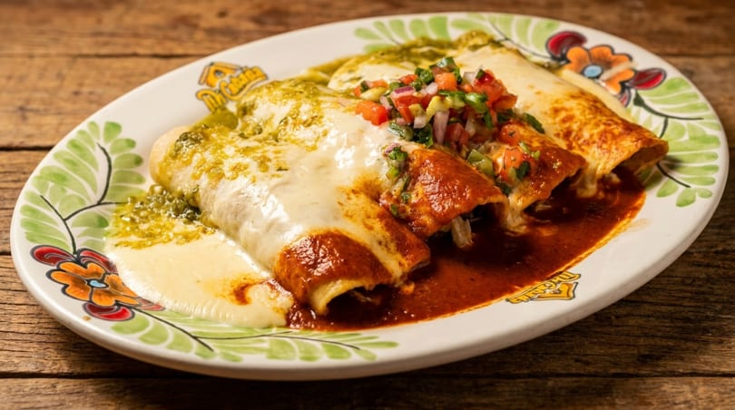 Three enchiladas, two with red sauce and one with green sauce, topped with cheese and pico de gallo.