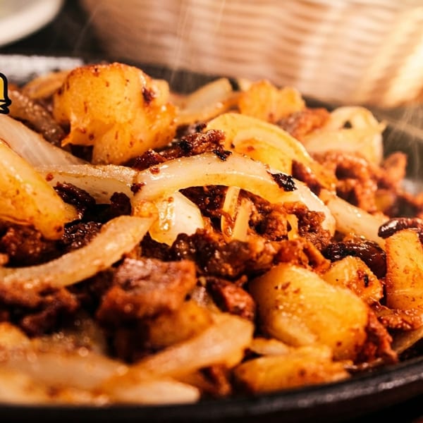 Sizzling Mi Cabaña Mexican Restaurants fajitas with steak, onions, and potatoes on a hot skillet.